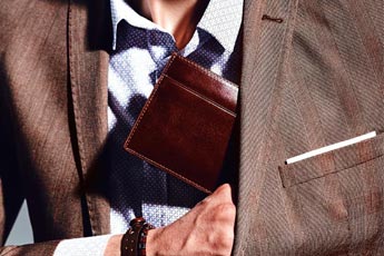 Homem a guardar uma bela carteira de couro castanho no bolso do seu fato - categoria carteiras de homem.